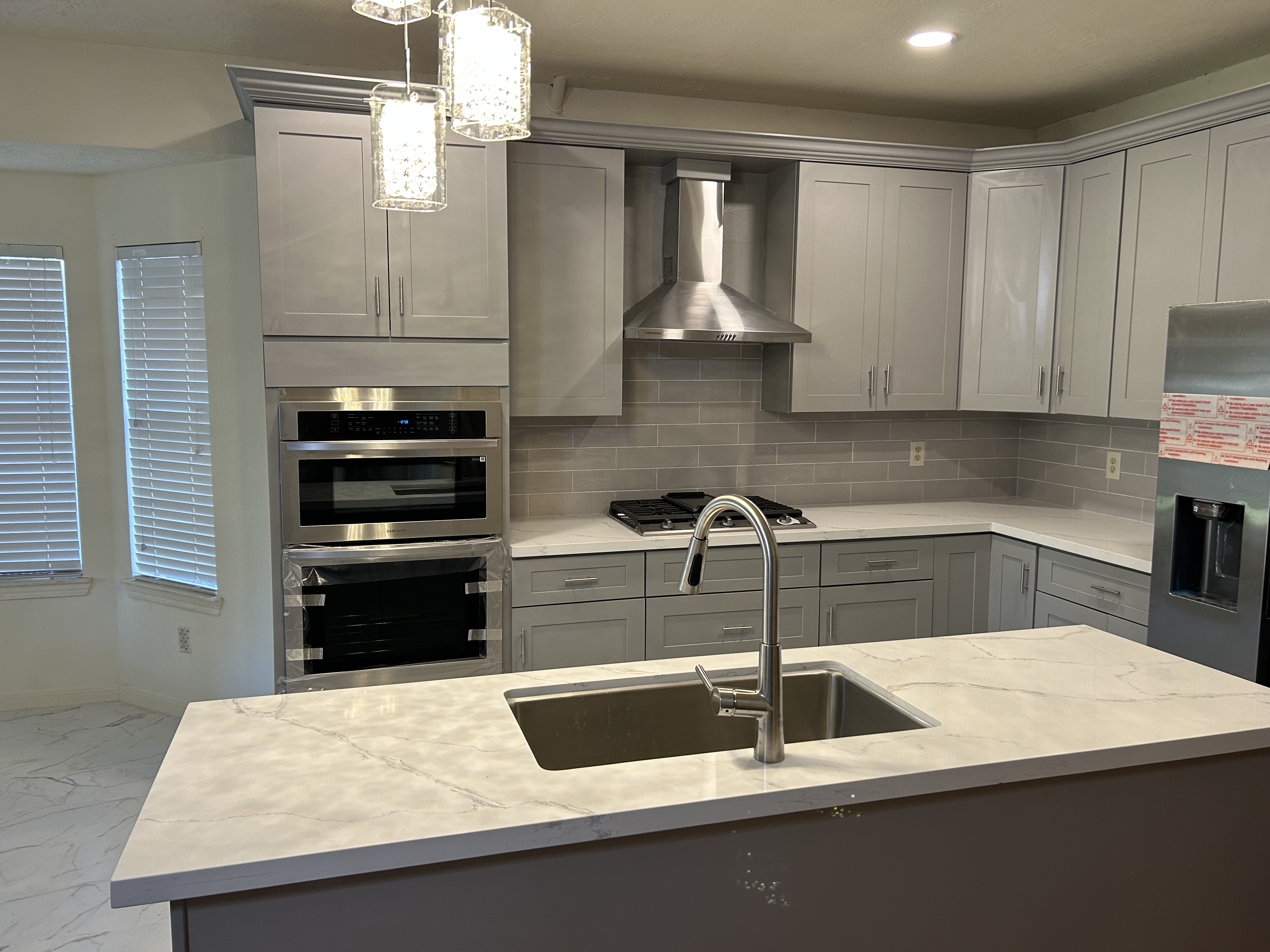 Finished kitchen in Cypress, Texas: gray flat-panel cabinetry, quartz waterfall island, tile backsplash and pendant lighting.